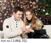 Молодая пара с белой чашкой сидит на диване на фоне новогодней елки и боке. Стоковое фото, фотограф Дарья Петренко / Фотобанк Лори