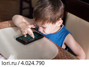 Мальчик за столом в общественной столовой играет в игры на смартфоне (2012 год). Редакционное фото, фотограф Родион Власов / Фотобанк Лори