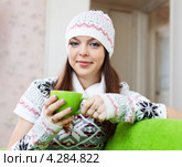 Девушка в свитере, шапке и митенках согревается горячим чаем на диване. Стоковое фото, фотограф Яков Филимонов / Фотобанк Лори