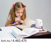 Девочка листает книгу и пишет на листе бумаги конспект сидя за столом (2013 год). Редакционное фото, фотограф Иванов Алексей / Фотобанк Лори