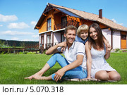 Молодая счастливая семья сидит на зелёной лужайке перед домом. Стоковое фото, фотограф Raev Denis / Фотобанк Лори