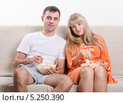 Молодая пара сидит на диване, ест попкорн и смотрит телевизор. Стоковое фото, фотограф Иванов Алексей / Фотобанк Лори