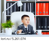 Маленький бизнесмен. Мальчик в костюме сидит перед ежедневником и чашкой кофе в офисе. Стоковое фото, фотограф Петр Малышев / Фотобанк Лори