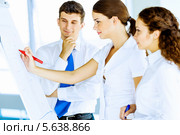 Молодые люди готовят проект. Улыбающаяся девушка пишет красным маркером на флипчарте, коллеги стоят рядом. Стоковое фото, фотограф Sergey Nivens / Фотобанк Лори