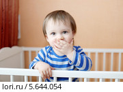 Малыш показывает, что он закрыл рот и молчит, стоя в кроватке. Стоковое фото, фотограф ivolodina / Фотобанк Лори