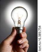 Mans hand holding a light bulb against grey background. Стоковое фото, агентство Ingram Publishing / Фотобанк Лори