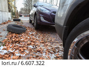 Автомобили во время замены резины на зимнюю во дворе дома с осенней листвой на земле. Стоковое фото, фотограф Кекяляйнен Андрей / Фотобанк Лори
