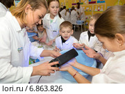 Врач проверяет микробы на руках у детей на детской интерактивной выставке "Стань врачом вместе с ЕМИАС" на ВДНХ в городе Москве, Россия (2015 год). Редакционное фото, фотограф Николай Винокуров / Фотобанк Лори