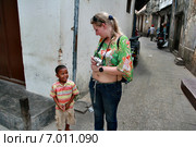 Black child local resident island of Zanzibar communicates with tourist  Стоун Таун - Каменный город на острове Занзибар в Танзании шестилетний арабский мальчик встретил на узкой улочке старого города, европейскую женщину блондинку с оголенным животом (2008 год). Редакционное фото, фотограф Владимир Григорьев / Фотобанк Лори