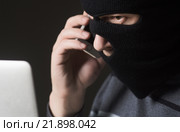 Преступник в маске разговаривает по мобильному и смотрит в ноутбук. Стоковое фото, фотограф Mark Agnor / Фотобанк Лори