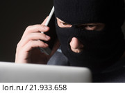 Хакер в маске сидит перед ноутбуком и разговаривает по мобильному. Стоковое фото, фотограф Mark Agnor / Фотобанк Лори
