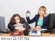 Девушка в офисе с улыбкой показывает время на часах рядом с обессиленной коллегой. Стоковое фото, фотограф Иванов Алексей / Фотобанк Лори