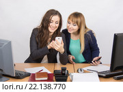 Две фисные работницы увлеченно смотрят в мобильный телефон за рабочем столом. Стоковое фото, фотограф Иванов Алексей / Фотобанк Лори