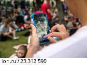 Молодой человек играет на мобильном телефоне в игру Pokemon Go от компании Niantic в Ильинском сквере города Москвы, Россия (2016 год). Редакционное фото, фотограф Николай Винокуров / Фотобанк Лори