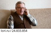 Old man sitting on the couch at home talking on smartphone. Стоковое видео, видеограф Сергей Кальсин / Фотобанк Лори