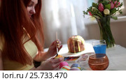 Redhead girl paints Easter eggs with a brush. on the table Easter cake, eggs, sweets, bouquet of flowers. Стоковое видео, видеограф Dmitry Chapurin / Фотобанк Лори