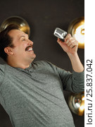 Smiling man with mustache poses with microphone in studio with lamps on wall. Стоковое фото, фотограф Losevsky Pavel / Фотобанк Лори