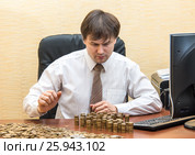 Мужчина в офисе за столом считает монеты и складывает их столбиками. Стоковое фото, фотограф Гетманец Инна / Фотобанк Лори
