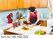 Молодая женщина в кухонном фартуке и шапочке пропитывает корж праздничного торта. Стоковое фото, фотограф Сергей Дубров / Фотобанк Лори