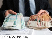 Бизнесмен сидит за столом с документами и держит в руках деньги. Стоковое фото, фотограф Игорь Низов / Фотобанк Лори