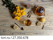 Useful herbal tea with a plant (Sideritis scardica) or Greek mountain tea with lemon in a cup and yellow chrysanthemums on a wooden table  close-up. Стоковое фото, фотограф Татьяна Ляпи / Фотобанк Лори