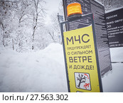 Табличка МЧС с оранжевым маячком-мигалкой, символьными знаками и картинками с предупреждением о сильном ураганном ветре и прочих опасностях и рисках для здоровья при плохой погоде. Предупреждение МЧС. Опасность падения заснеженных деревьев. Снег и лед на деревьях. Парк "Сокольники" (2018 год). Редакционное фото, фотограф Mikhail Leonov / Фотобанк Лори
