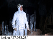 Potholer in white overalls among ice stalagmites in a cave on a dark background. Стоковое фото, фотограф Евгений Харитонов / Фотобанк Лори