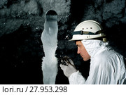 Speleologist in a cave examines a giant ice stalagmite covered with hoarfrost, against a background of a dark rock covered with ice crystals. Стоковое фото, фотограф Евгений Харитонов / Фотобанк Лори