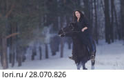 Beautiful longhaired woman riding a black horse through the snow in the forest, stallion prancing. Стоковое фото, фотограф Константин Шишкин / Фотобанк Лори