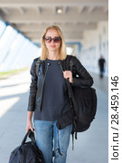Portrait of young cheerful female traveler wearing casual clothes carrying heavy backpack and luggage at airport. Стоковое фото, фотограф Matej Kastelic / Фотобанк Лори