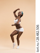 Full-length portrait of a sporty young cheerful african woman standing on beige background. Стоковое фото, агентство Ingram Publishing / Фотобанк Лори