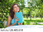 Positive adult beautiful woman sitting near table and reading book outdoors at backyard in summer. Стоковое фото, фотограф Kirill Kedrinskiy / Ingram Publishing / Фотобанк Лори