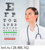 Female optician standing in front of eyesight test at hospital. Стоковое фото, фотограф Kirill Kedrinskiy / Ingram Publishing / Фотобанк Лори