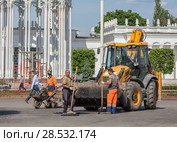 Москва, ВДНХ. Реконструкция 2017-2018 года. Рабочие - асфальтоукладчики стоят рядом с большим желтым трактором, оснащенным ковшом, на главной аллее. Редакционное фото, фотограф Наталья Николаева / Фотобанк Лори