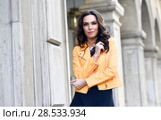 Young brunette woman, model of fashion, wearing orange modern jacket and blue skirt. Pretty caucasian girl with long wavy hairstyle. Female in urban background. Стоковое фото, фотограф Javier Sánchez Mingorance / Ingram Publishing / Фотобанк Лори