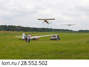 Glider being towed into the sky by light aircraft. Automobile towing glider on the airfield for the takeoff point. People accompany glider. Man supports the wing trailed along the ground glider (2017 год). Редакционное фото, фотограф Наталья Николаева / Фотобанк Лори