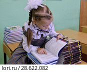 Девочка внимательно рассматривает новые учебники в классе, сидя на парте (2012 год). Редакционное фото, фотограф Илюхина Наталья / Фотобанк Лори
