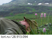 Tired traveler in the mountains - a man in a hat and travel clothes resting, lying on his back in the alpine meadow on a mountain plateau. Стоковое фото, фотограф Евгений Харитонов / Фотобанк Лори