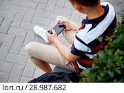 Child sitting outside school and playing games on his cell phone. Стоковое фото, фотограф Евгений Глазунов / Фотобанк Лори