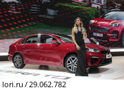 Московский автосалон 2018 года, девушка модель у красного автомобиля KIA на фоне рекламного видеоролика. Редакционное фото, фотограф Дмитрий Неумоин / Фотобанк Лори