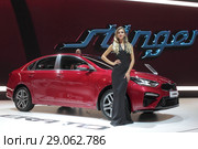 Московский автосалон 2018 года, девушка модель у красного автомобиля KIA на фоне рекламного видеоролика. Редакционное фото, фотограф Дмитрий Неумоин / Фотобанк Лори
