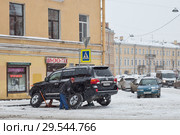 Мужчина меняет колеса на шиномонтаже во время снегопада в Санкт-Петербурге (2017 год). Редакционное фото, фотограф Евгений Кашпирев / Фотобанк Лори