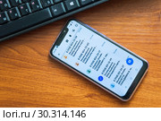 Смартфон с мошенническими смс сообщениями лежит на столе рядом с компьютерной клавиатурой (2019 год). Редакционное фото, фотограф Алёшина Оксана / Фотобанк Лори