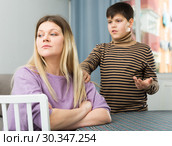 Upset mother sitting at table after arguing with son indoors. Стоковое фото, фотограф Яков Филимонов / Фотобанк Лори