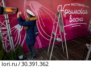 Посетитель фестиваля греет руки у обогревателя на сцене на площадке фестиваля "Крымская весна" на Манежной площади в городе Москве, Россия (2019 год). Редакционное фото, фотограф Николай Винокуров / Фотобанк Лори