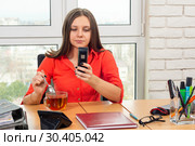 Сотрудница офиса пьет чай на рабочем месте, и набирает номер телефона. Стоковое фото, фотограф Иванов Алексей / Фотобанк Лори