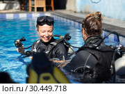 Woman getting first experience with scuba diving under the guidance of experienced recreational diving instructor in swimming pool. Стоковое фото, фотограф Matej Kastelic / Фотобанк Лори
