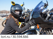 Biker girl in helmet and mask embracing plastic front cowl with headlight of her motorcycle, looking at camera. Стоковое фото, фотограф Кекяляйнен Андрей / Фотобанк Лори