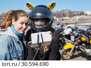 Счастливые и улыбающиеся женщины-мотоциклисты делают селфи с помощью смартфона с раздвижным моноподом. Фокус на смартфоне. Стоковое фото, фотограф Кекяляйнен Андрей / Фотобанк Лори