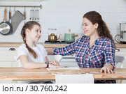 Счастливые и улыбающиеся дочь и мать, разговаривающие сидя за столом на кухне. Стоковое фото, фотограф Кекяляйнен Андрей / Фотобанк Лори